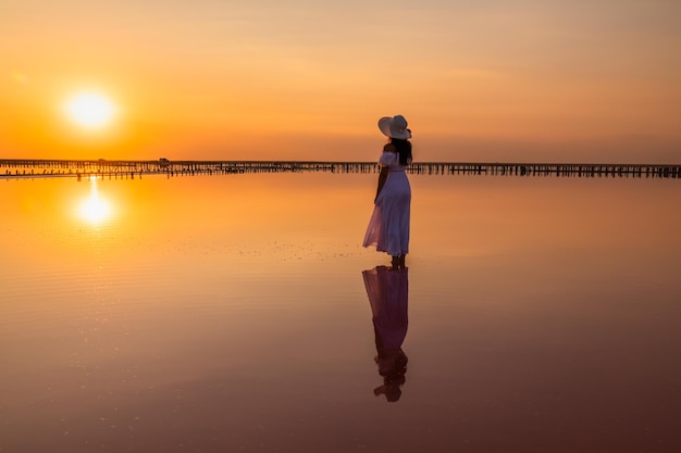 Vrouw in een witte jurk bij zonsondergang op een roze zoutmeer Reflectie zonsondergang in water