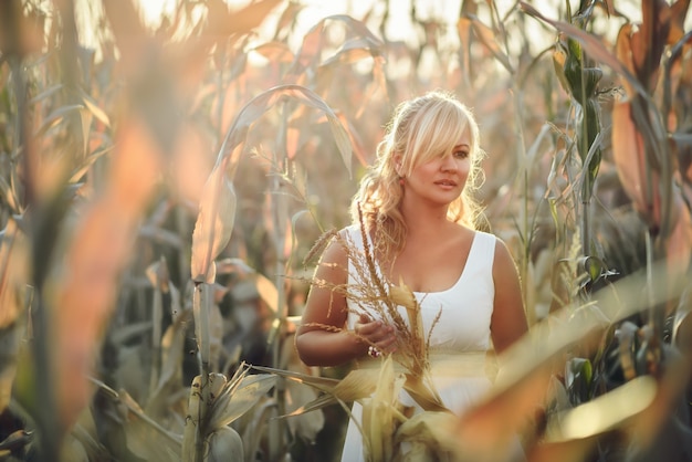 Vrouw in een witte lange zomerjurk loopt op een korenveld en poseert in zonsondergangtijd.