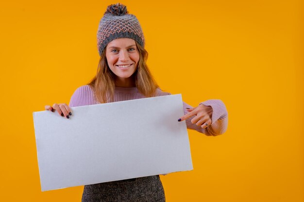 Foto vrouw in een wollen muts met een wit bord op een gele achtergrond