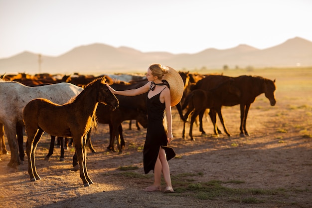 Vrouw in een zwarte jurk onder wilde paarden