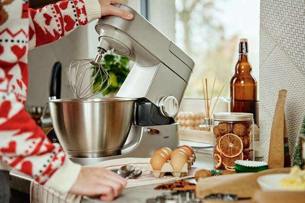 Vrouw in feestelijke kerstsweater die deeg voorbereidt voor koekjes thuis keuken vrouwelijke handen gebruiken elec