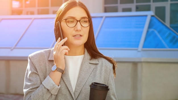 Vrouw in formeel pak praten aan de telefoon en koffie drinken op straat.