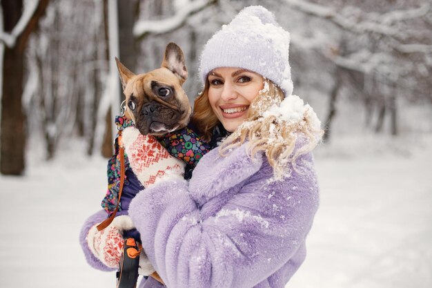 Vrouw in gebreide muts spelen met haar hond Franse bulldog op een sneeuw