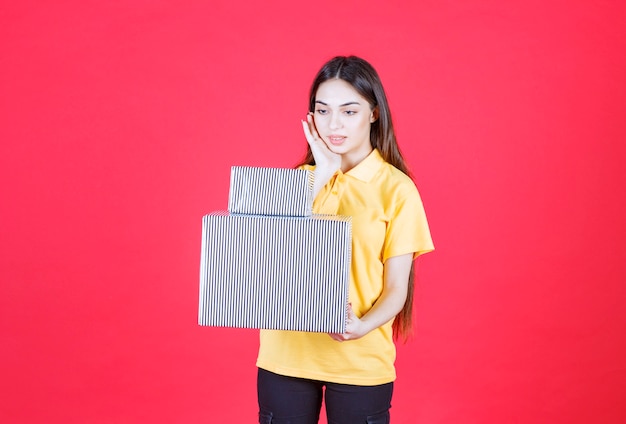 vrouw in geel shirt met grote en kleine zilveren geschenkdozen en ziet er attent uit.