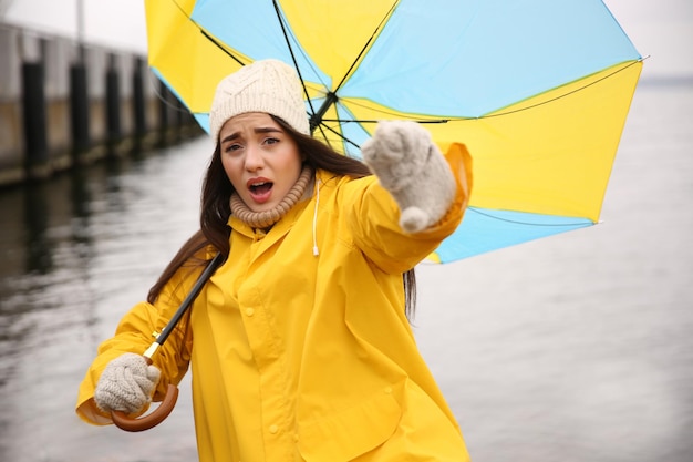 Vrouw in gele regenjas met paraplu gevangen in windvlaag in de buurt van rivier