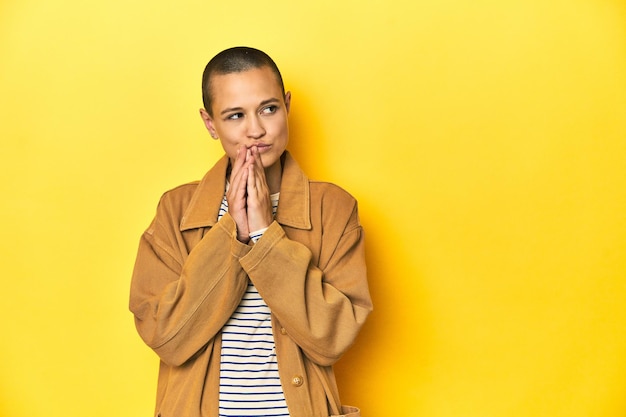 Vrouw in gestreepte T-shirt en denim shirt gele achtergrond die een plan in gedachten heeft en een idee opstelt