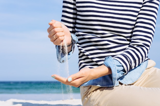 Vrouw in gestreepte T-shirt op het strand giet zand in haar hand