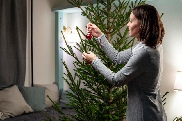 vrouw in gezellig huis houdt een rode bal in haar handen en begint de kerstboom te versieren