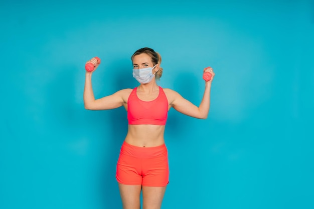 Vrouw in gezichtsbeschermingsmasker en fitnesskleding geïsoleerd over blauwe achtergrond