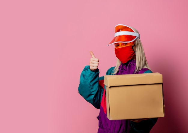 Vrouw in gezichtsmasker en kleding uit de jaren 80 met bezorgdoos op roze