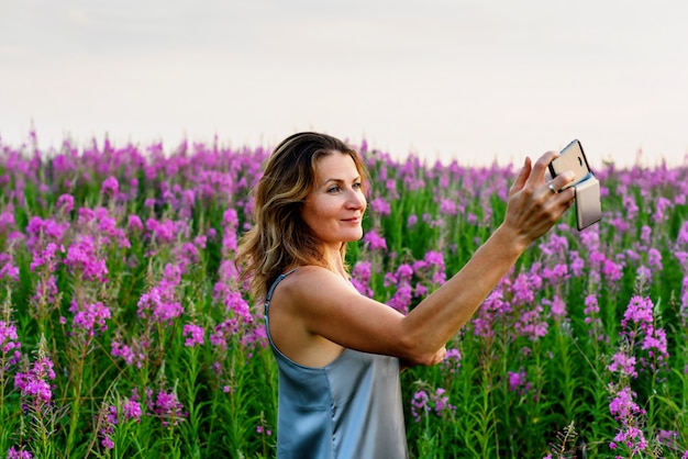 Vrouw in grijze jurk neemt selfie foto op mobiel op wilgenroosje weide