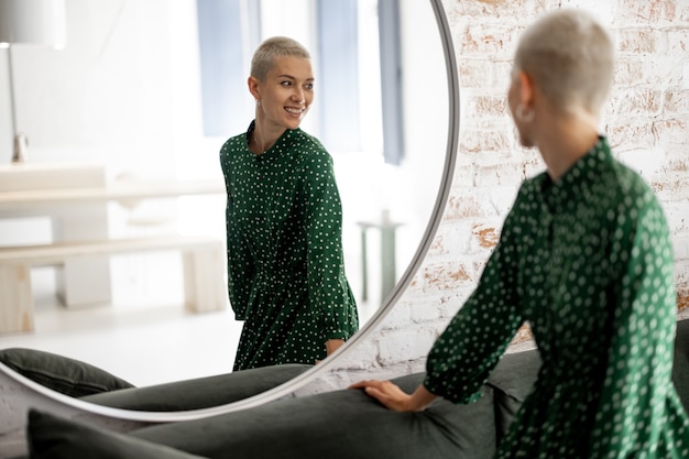 Vrouw in groene jurk kijkt thuis naar zichzelf in de spiegel