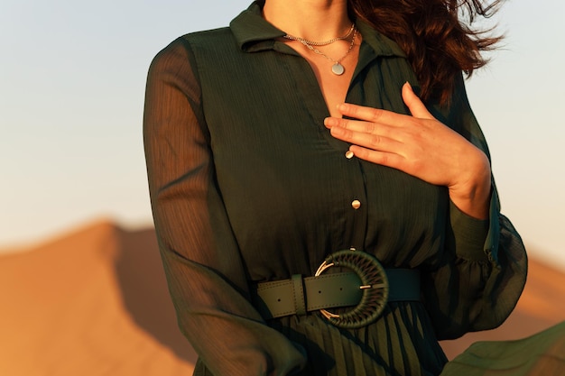 Vrouw in groene lange jurk staat in woestijnzandduinen achtergrond geeloranje zonsondergang