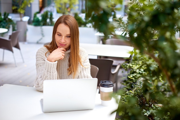 Vrouw in grote trui luistert aandachtig of studeert op afstand op caféterras