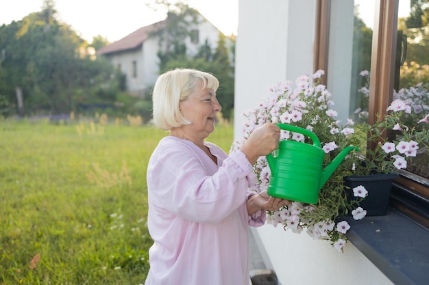 Vrouw in haar tuin water met een blauwe waterblik van gekleurde bloemen om kleur te geven en te versieren