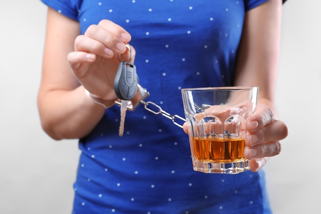 Vrouw in handboeien met glas alcohol en autosleutel tegen lichte achtergrond Drink niet en rijd concept