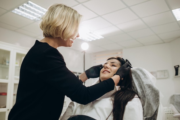 Vrouw in handschoenen die zich voorbereiden op de permanente make-up van het voorhoofd met een liniaal