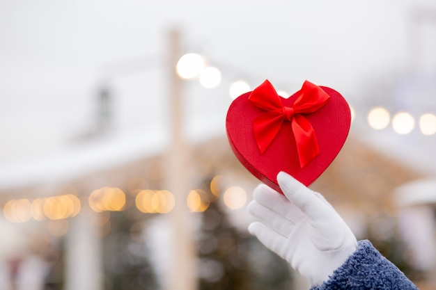 Vrouw in handschoenen met een hartvormige geschenkdoos met een zijden lint op straat. Ruimte voor tekst