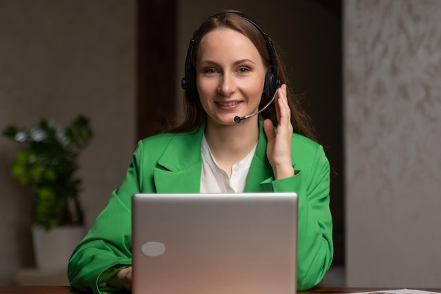 Vrouw in headset praat met cliënt die in de buurt van opengeklapte laptop zit aan tafel in kantoor jonge vrouwelijke consultant
