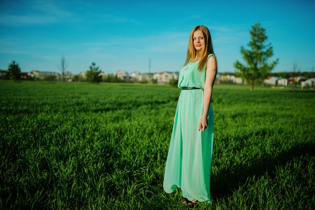 Vrouw in het mooie lange turkooise kleding stellen op een weide