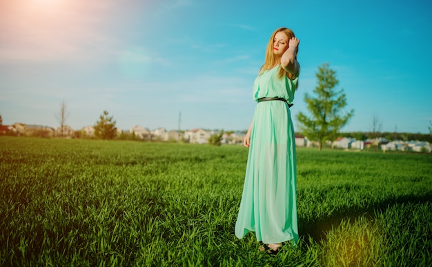 Vrouw in het mooie lange turkooise kleding stellen op een weide