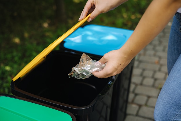 Vrouw in het park gooit plastic zak in de prullenbak in verschillende kleuren op plastic bakken groen