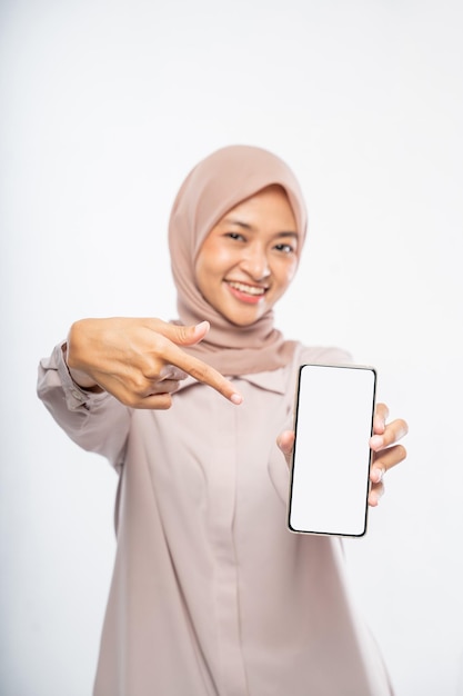 Vrouw in hijab die lacht terwijl ze een mobiele telefoon gebruikt die een leeg scherm toont aan de camera