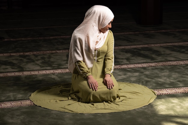 Vrouw in hijab zittend in moskee en biddend
