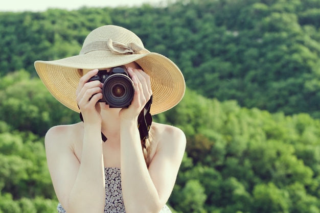 vrouw in hoed maakt foto's tegen het groene bos. Vooraanzicht