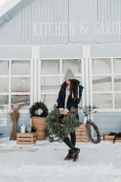 Vrouw in interdoek houdt een natuurlijke krans buiten bij het blauwe huis.