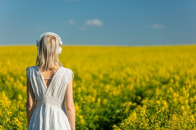 Vrouw in jurk met koptelefoon in koolzaad veld