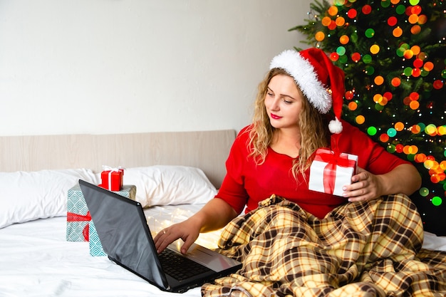 Vrouw in Kerstman hoed houdt dozen met geschenken in de buurt van de kerstboom