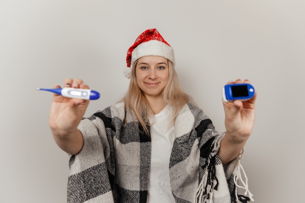 Vrouw in kerstmuts en beschermend medisch masker houdt thermometer en pulsoximeter vast