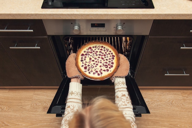 Vrouw in kersttrui haalt frambozen shortcake uit de oven.