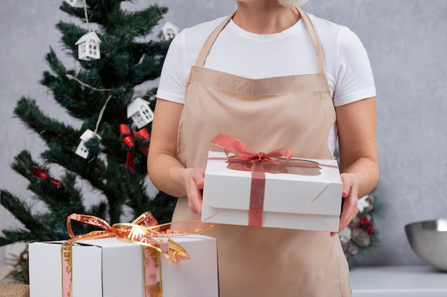 Vrouw in keuken kleed houdt geschenkdozen met kerstsnoepjes. zoete cadeaus voor het nieuwe jaar.