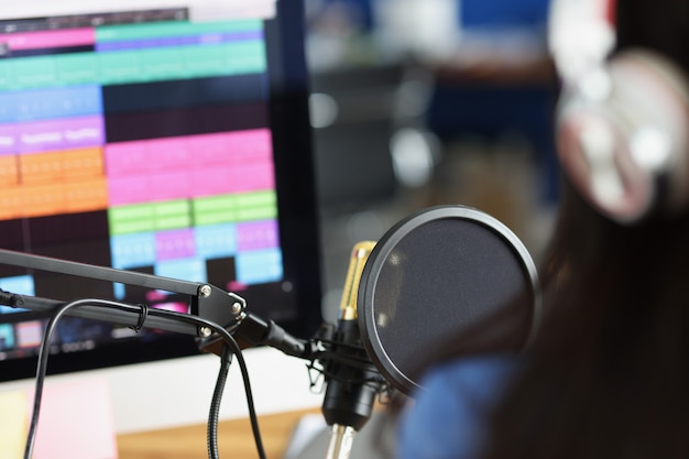 Vrouw in koptelefoon voor microfoon kijkt naar monitor met soundtrack radiopresentator