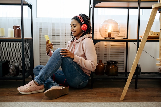 Vrouw in koptelefoon zittend op de vloer en luisteren naar muziek van mobiele telefoon. Mooie dame in oortelefoons ontspant in de kamer, vrouwelijke geluidsliefhebber rust