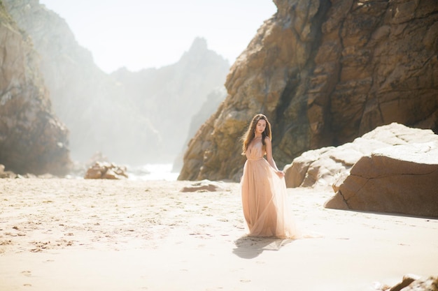 Vrouw in lange jurk in de buurt van rotsen en oceaan