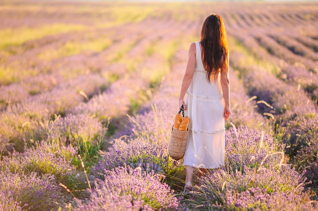 Vrouw in lavendel bloemen veld bij zonsondergang in witte jurk en hoed