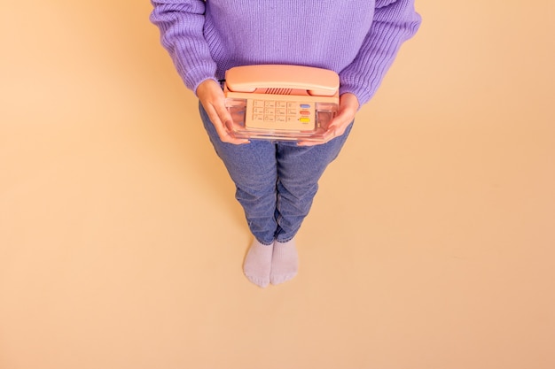 Vrouw in lila trui, jeans en sokken met een telefoon. Beige achtergrond.