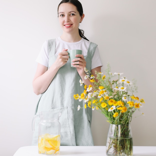 Vrouw in linnen schort limonade drinken met gezellig huis