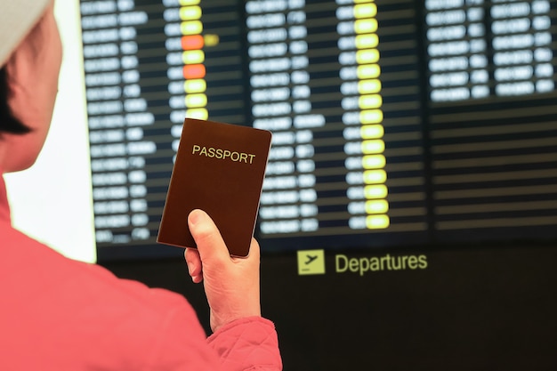 Vrouw in luchthaven met paspoort in haar hand, kijkend naar het vluchtinformatiebord