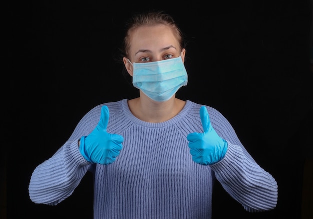 Vrouw in medisch gezichtsmasker en handschoenen verschijnt duim op zwarte muur.