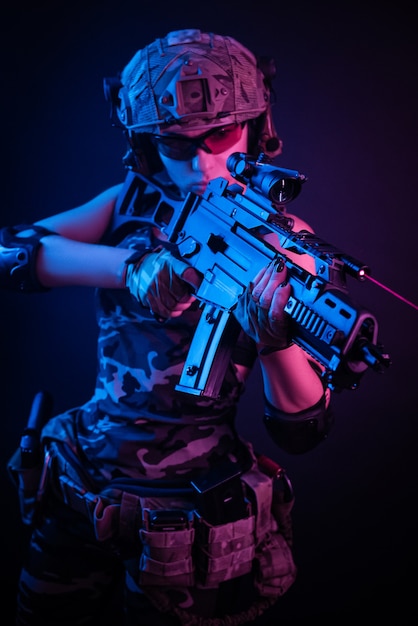 Vrouw in militaire overall airsoft poseren met een pistool in zijn handen op een donkere muur in de nevel in neonlicht