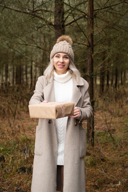 Vrouw in mode warme kleren met geschenkdoos in kraftpapier verpakking op natuur achtergrond