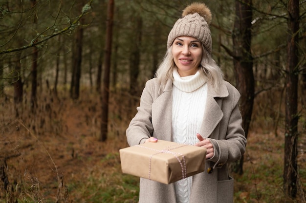 Vrouw in mode warme kleren met geschenkdoos in kraftpapier verpakking op natuur achtergrond
