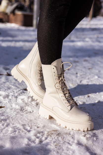 Vrouw in modieuze witte laarzen op witte sneeuw close-up Damesbenen in stijlvolle winter leren laarzen