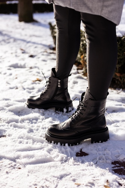 Vrouw in modieuze zwarte laarzen op witte sneeuw close-up Womens benen in stijlvolle winter lederen laarzen