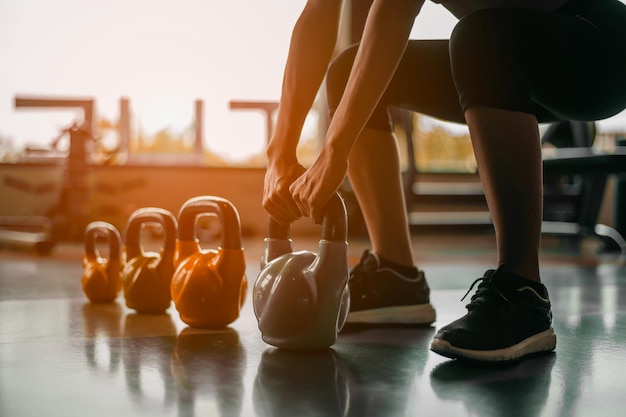 Vrouw in oefeningsuitrusting die op een rij staat met halters tijdens een oefeningsles in de sportschool. Fitnesstraining met kettlebell in sportgymnastiek.