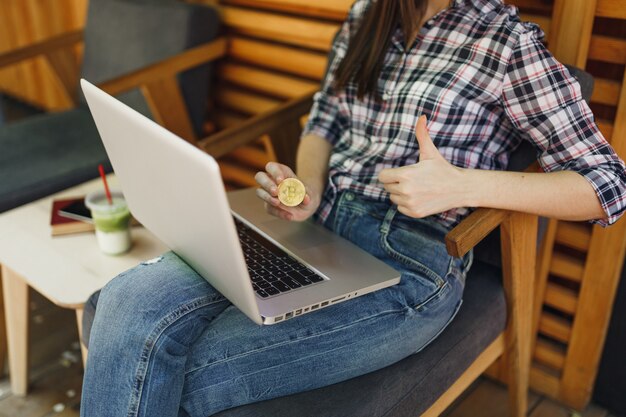 Vrouw in openlucht straat coffeeshop café zit met laptop pc computer, houd bitcoin, metalen munt van gouden kleur